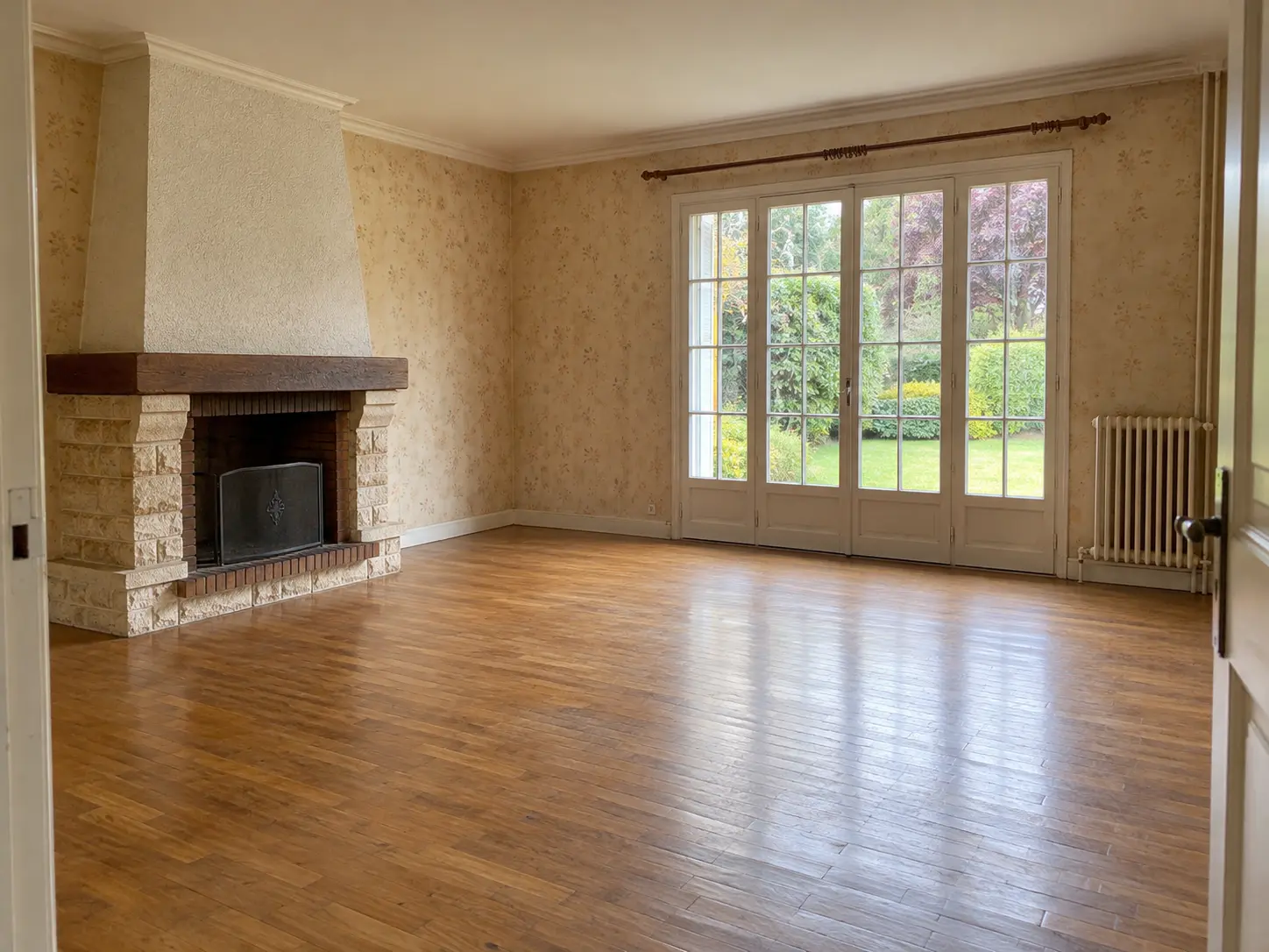 Salon vide d’une maison ancienne avec parquet, papier peint et cheminée